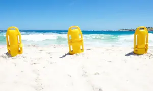 Trzy żółte bojki ratownicze stoją na piaszczystej plaży, z morzem i niebem w tle.