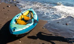 Niebiesko-żółty kajak pneumatyczny z wiosłami na piaszczystej plaży przy falującej wodzie.