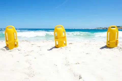 Trzy żółte bojki ratownicze stoją na piaszczystej plaży, z morzem i niebem w tle.