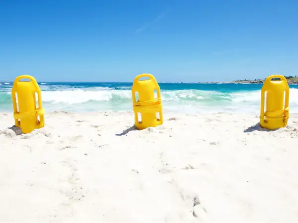 Trzy żółte bojki ratownicze stoją na piaszczystej plaży, z morzem i niebem w tle.